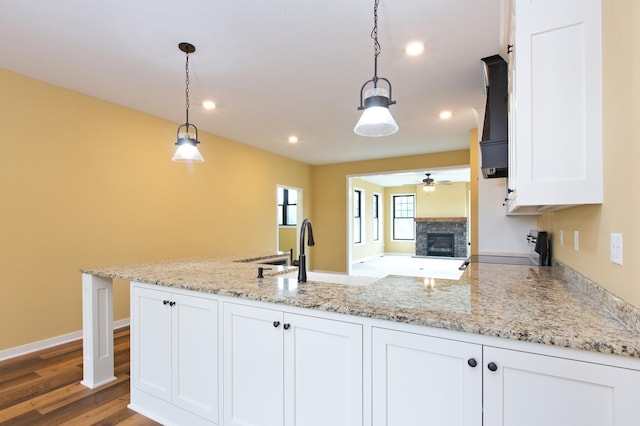 kitchen with pendant lighting, a fireplace, ceiling fan, white cabinetry, and dark hardwood / wood-style floors