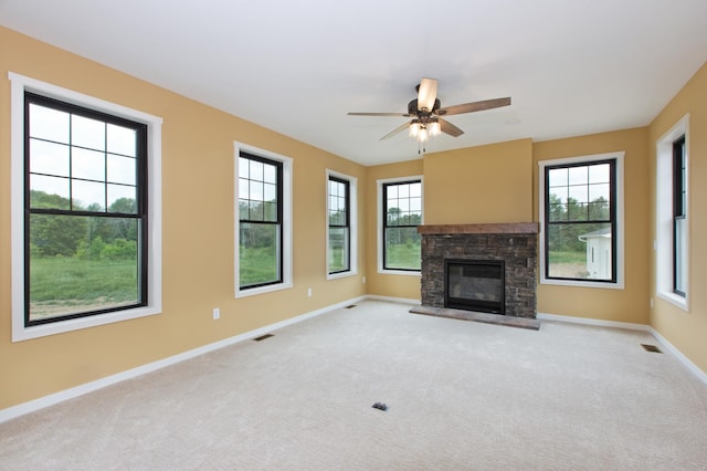 unfurnished living room with ceiling fan, light carpet, and a stone fireplace