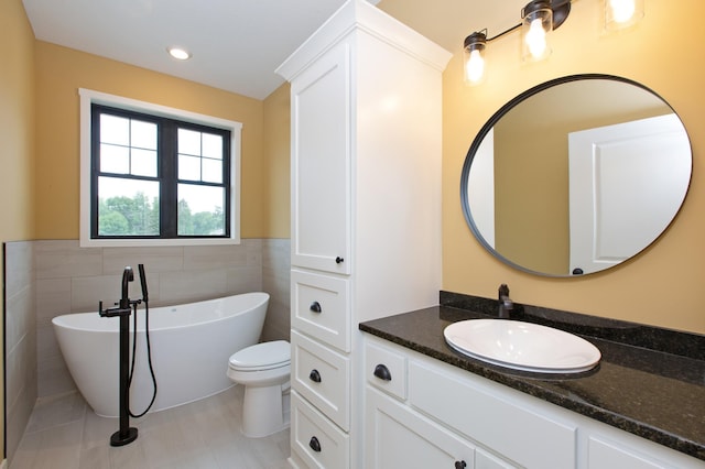 bathroom with tile walls, toilet, vanity with extensive cabinet space, a bath to relax in, and tile flooring