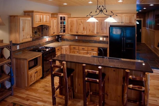 kitchen with an island with sink, a kitchen bar, sink, light hardwood / wood-style flooring, and black appliances