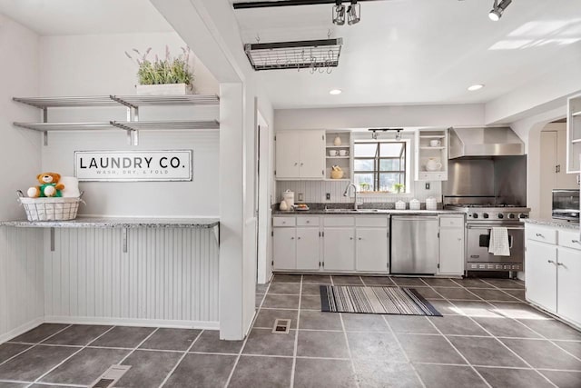 kitchen with dark tile flooring, wall chimney exhaust hood, white cabinets, and appliances with stainless steel finishes