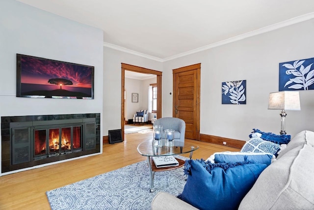 living room featuring crown molding, a tile fireplace, and light wood-type flooring