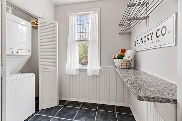 washroom with stacked washer / dryer and dark tile floors