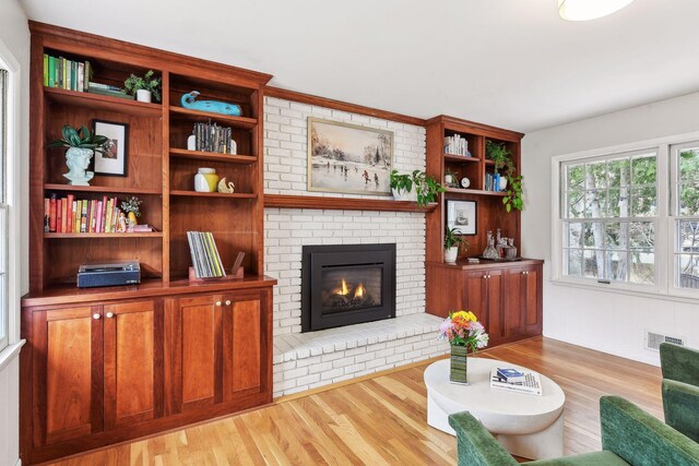 living room with brick wall, a brick fireplace, and light hardwood / wood-style flooring