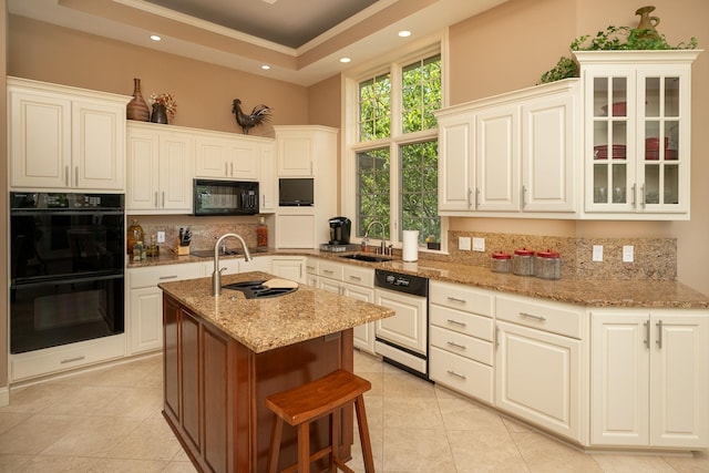 kitchen with light stone counters, sink, black appliances, a center island with sink, and white cabinetry