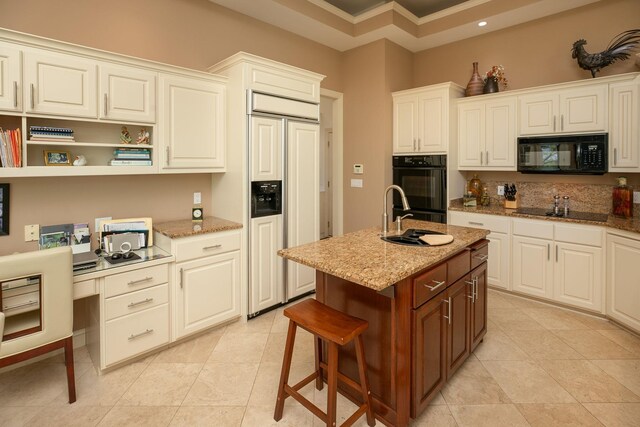 kitchen with light stone counters, a kitchen island with sink, sink, black appliances, and white cabinets