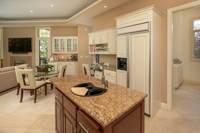 kitchen featuring paneled refrigerator, white cabinetry, a kitchen island with sink, and sink