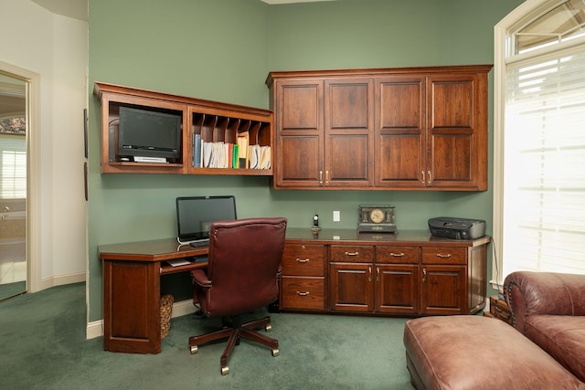 office featuring dark colored carpet, built in desk, and a healthy amount of sunlight