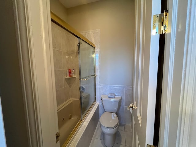 bathroom with tile patterned flooring, enclosed tub / shower combo, tile walls, and toilet