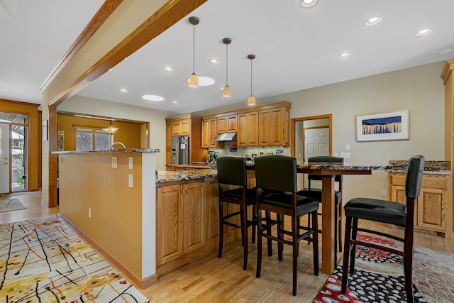 kitchen featuring stone countertops, pendant lighting, stainless steel fridge with ice dispenser, light hardwood / wood-style floors, and a kitchen bar