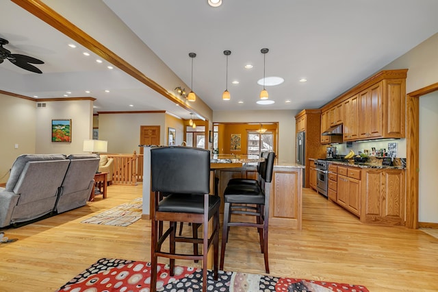 kitchen featuring high end appliances, ceiling fan, a breakfast bar area, and light hardwood / wood-style floors