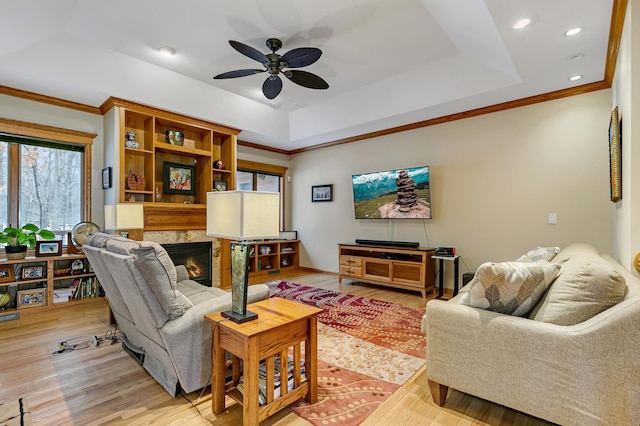 living room featuring a tray ceiling, ceiling fan, ornamental molding, and light hardwood / wood-style flooring