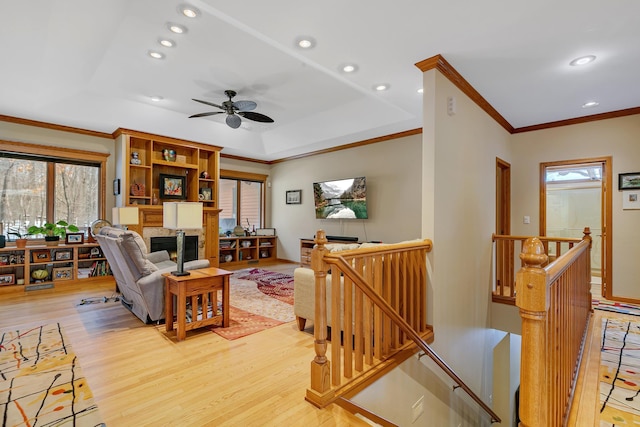 living room featuring a tray ceiling, ceiling fan, light hardwood / wood-style floors, and ornamental molding