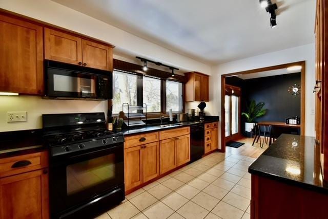 kitchen featuring dark stone countertops, track lighting, black appliances, sink, and light tile patterned flooring