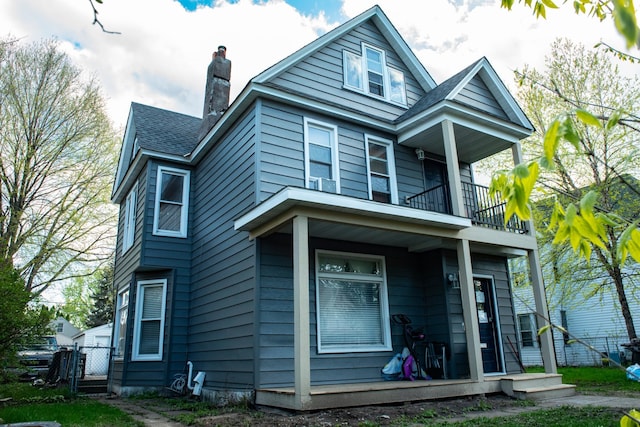view of front of home featuring fence, a balcony, a chimney, a shingled roof, and a porch