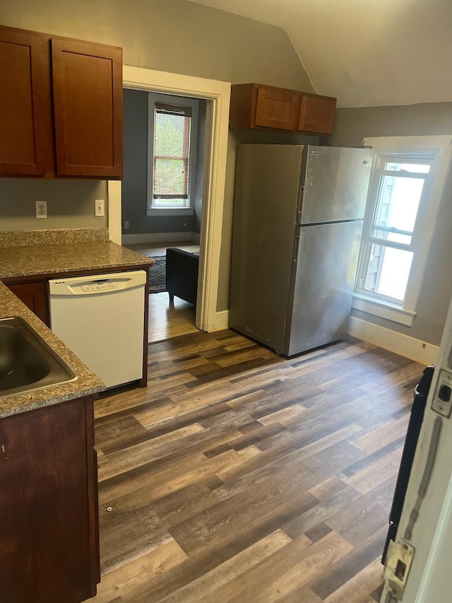 kitchen featuring dark stone countertops, vaulted ceiling, stainless steel refrigerator, dark hardwood / wood-style flooring, and white dishwasher