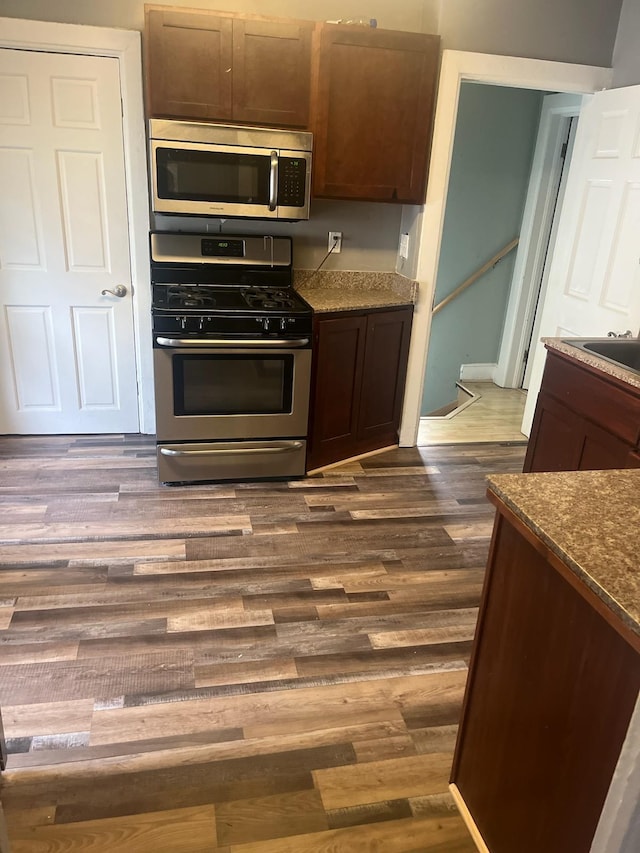 kitchen with dark stone counters, dark wood-style floors, dark brown cabinets, and stainless steel appliances