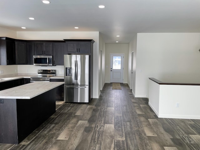 kitchen with appliances with stainless steel finishes, a kitchen island, and dark wood-type flooring