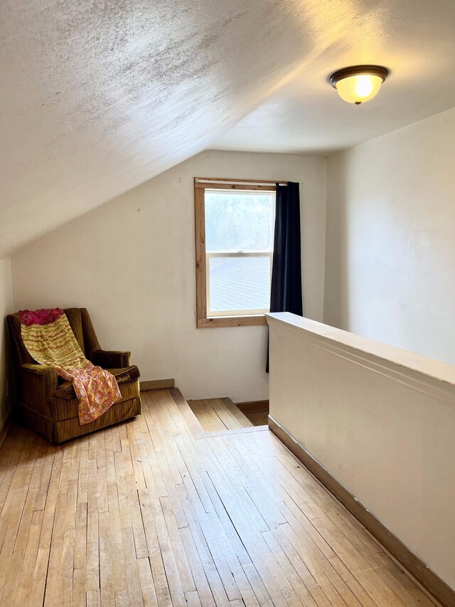 living area with vaulted ceiling, light hardwood / wood-style floors, and a textured ceiling