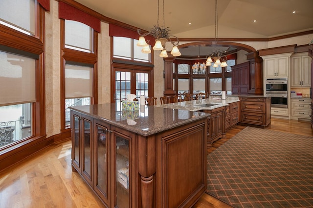 kitchen featuring hanging light fixtures, dark stone counters, a notable chandelier, light hardwood / wood-style flooring, and french doors