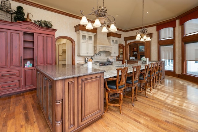 kitchen with dark stone counters, custom range hood, pendant lighting, a notable chandelier, and wood-type flooring