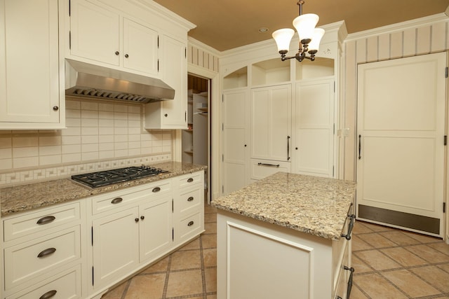 kitchen featuring an inviting chandelier, pendant lighting, backsplash, ornamental molding, and wall chimney exhaust hood