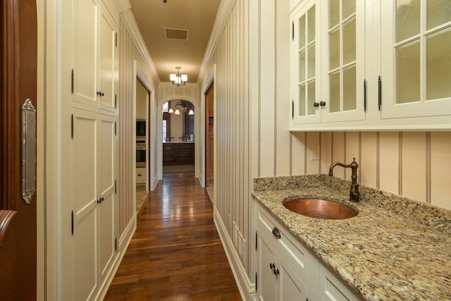 interior space with crown molding, a notable chandelier, sink, and dark wood-type flooring