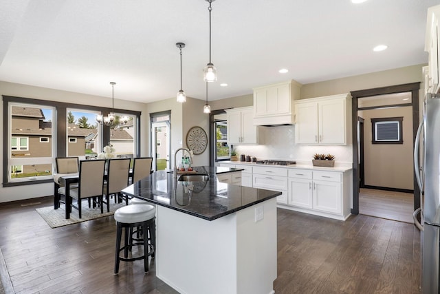 kitchen featuring hanging light fixtures, dark hardwood / wood-style floors, a center island with sink, and white cabinets