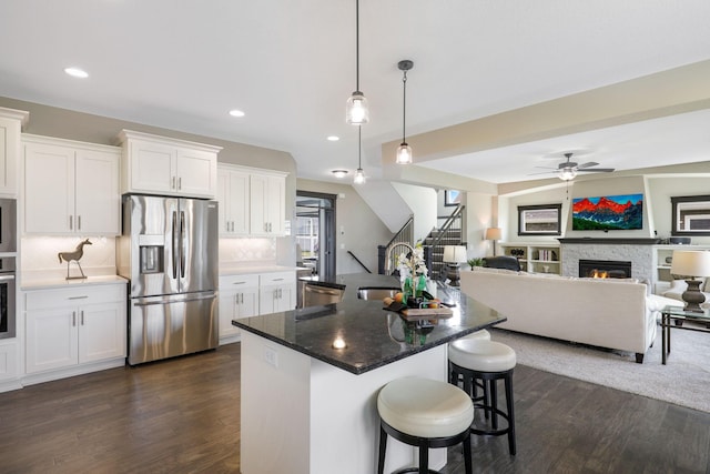 kitchen featuring stainless steel appliances, decorative light fixtures, tasteful backsplash, a stone fireplace, and dark hardwood / wood-style floors