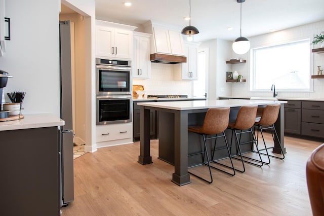 kitchen featuring decorative light fixtures, white cabinetry, double oven, a kitchen breakfast bar, and light hardwood / wood-style flooring