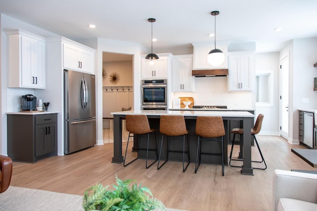 kitchen with stainless steel appliances, white cabinets, a kitchen island, pendant lighting, and light hardwood / wood-style flooring