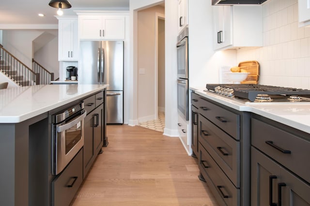 kitchen featuring decorative backsplash, light wood-type flooring, stainless steel appliances, white cabinets, and light stone counters