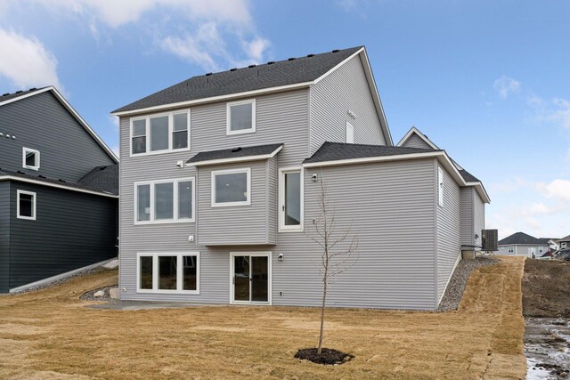 rear view of property featuring roof with shingles, central AC, and a yard