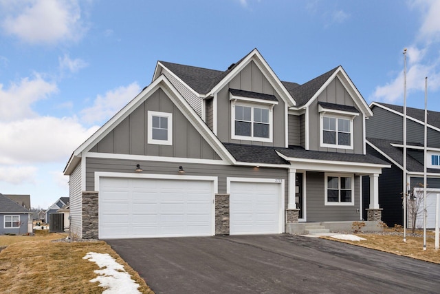 craftsman house featuring aphalt driveway, an attached garage, central AC, a shingled roof, and board and batten siding