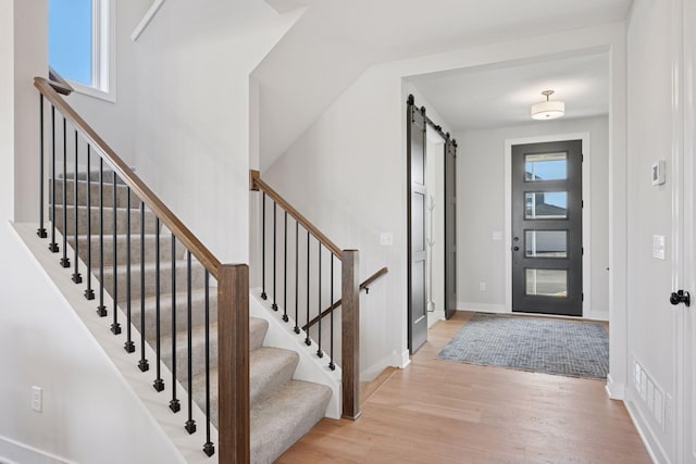 entryway with light wood-type flooring, a barn door, visible vents, and baseboards