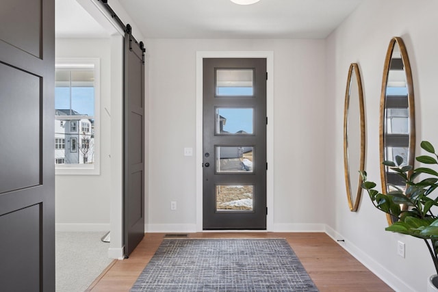 foyer entrance with visible vents, light wood-style flooring, baseboards, and a barn door