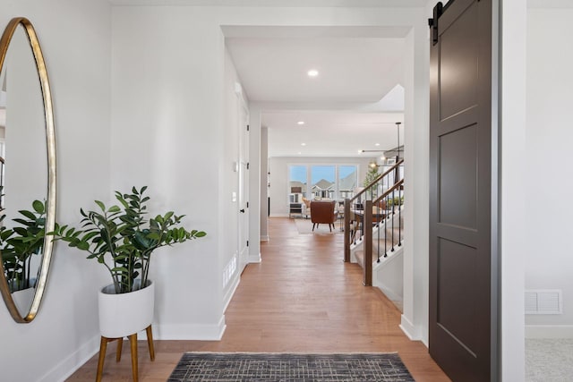 hallway featuring recessed lighting, light wood-style flooring, a barn door, baseboards, and stairs