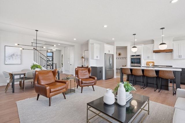 living room featuring recessed lighting, stairway, an inviting chandelier, light wood-style floors, and baseboards