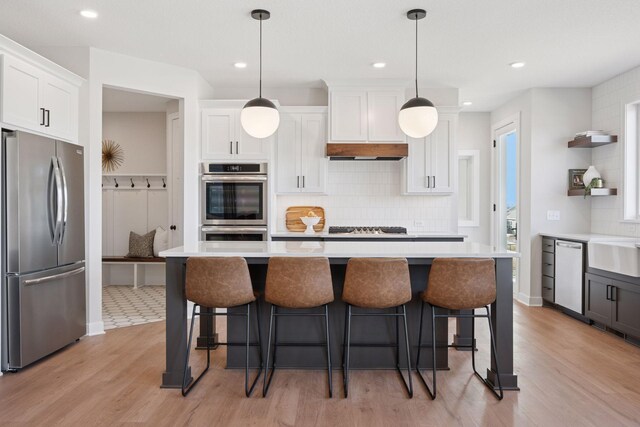 kitchen with stainless steel appliances, light countertops, white cabinetry, under cabinet range hood, and a kitchen bar