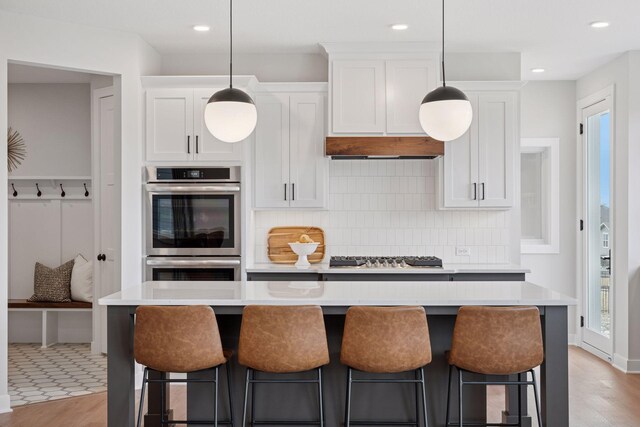 kitchen with tasteful backsplash, stainless steel appliances, light countertops, a kitchen bar, and white cabinetry