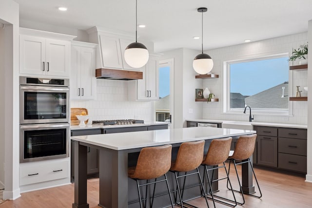 kitchen featuring open shelves, stainless steel appliances, light countertops, light wood-style floors, and a sink