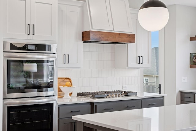 kitchen featuring gray cabinets, ventilation hood, stainless steel appliances, and backsplash