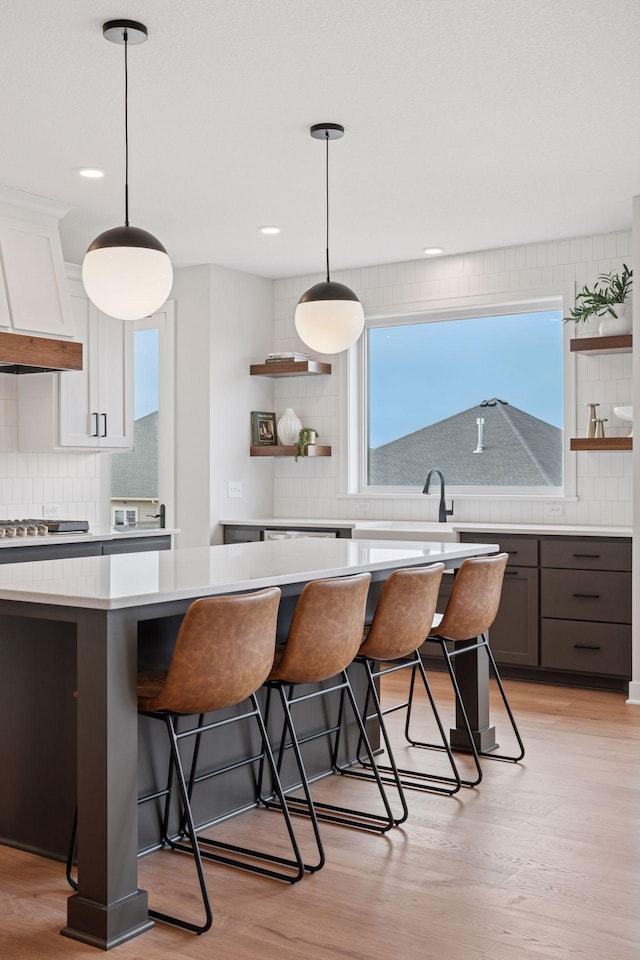 kitchen featuring open shelves, a kitchen bar, light countertops, and light wood-style flooring