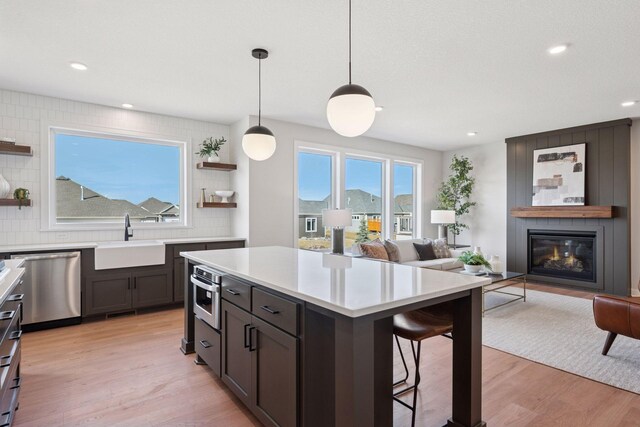 kitchen featuring a breakfast bar area, open shelves, stainless steel dishwasher, a large fireplace, and a sink