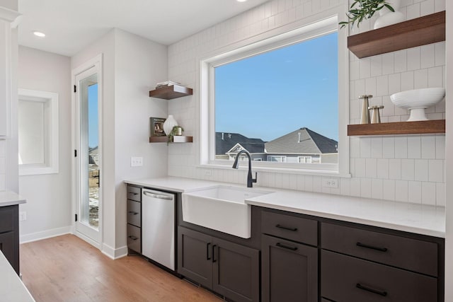 kitchen with open shelves, decorative backsplash, stainless steel dishwasher, light wood-style floors, and a sink