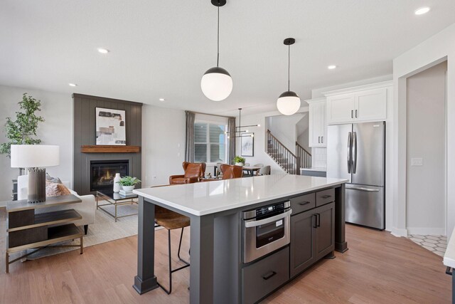 kitchen featuring a breakfast bar area, appliances with stainless steel finishes, a glass covered fireplace, light wood-style floors, and white cabinetry