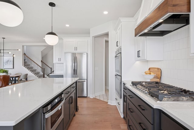 kitchen featuring decorative light fixtures, appliances with stainless steel finishes, white cabinets, and custom range hood