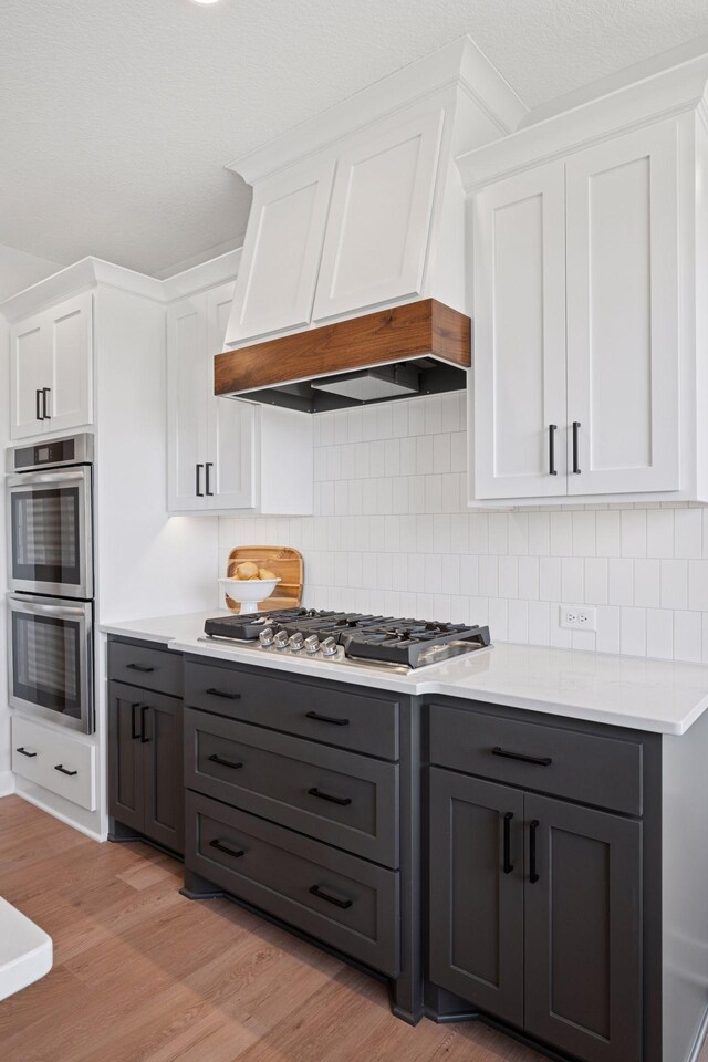 kitchen featuring light countertops, custom range hood, light wood-style flooring, gray cabinetry, and appliances with stainless steel finishes