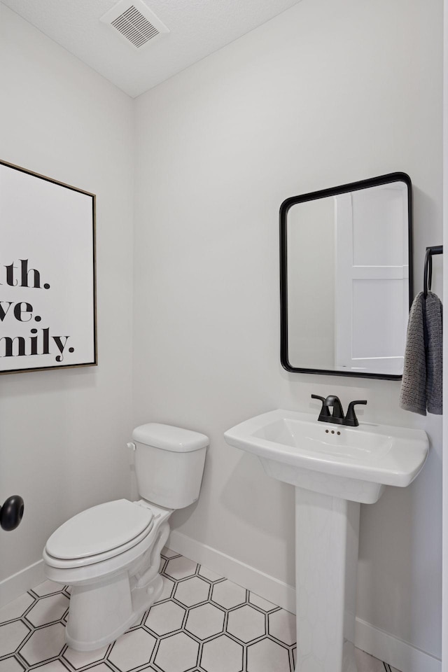 half bathroom with toilet, baseboards, visible vents, and a sink