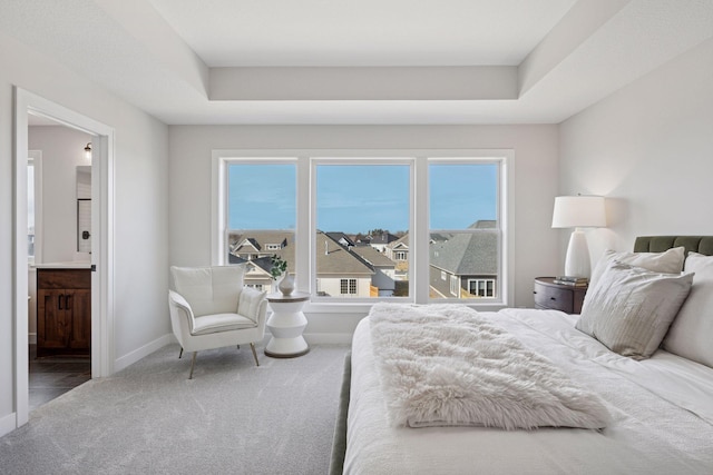 carpeted bedroom with ensuite bath, a raised ceiling, and baseboards